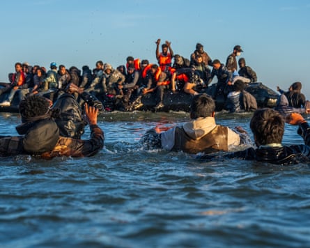 People seeking to get to the UK irregularly wade in deep water to board a dinghy into the Channel