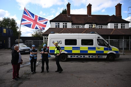 A man holding a large union flag speaks to three police officers standing in front of a police van