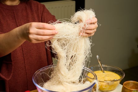 Closeup of two hands separating a bundle of kataifi pastry.