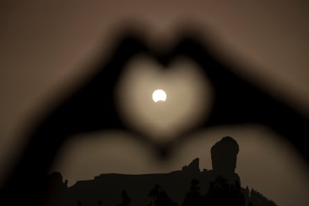 A woman makes a heart shape with her hands during a partial eclipse of the sun