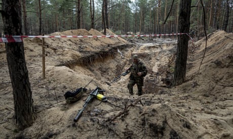A Ukrainian serviceman uses a metal detector to inspect a mass burial site in Izium, Ukraine