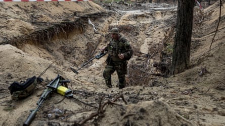 A Ukrainian serviceman uses a metal detector to inspect a mass grave in the recently retaken area of Izium, Ukraine,
