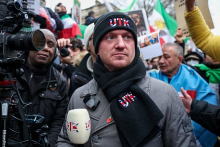 Tommy Robinson at a march wearing a black scarf and woolly hat with the letters UTK in a red, white and blue pattern like the union jack.