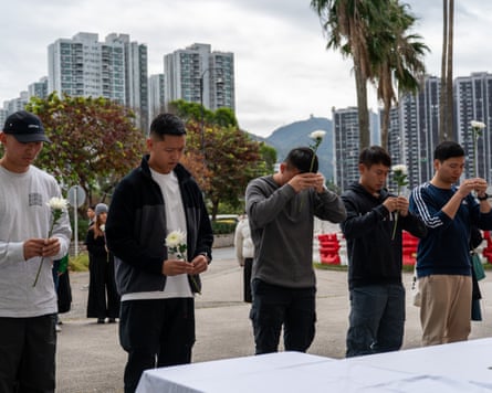 A line of mourners praying with the Hong Kong skyline in the background