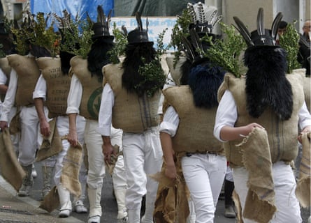 Men wearing masks of black badger hair, top hats crowned by feathers and sprays of boxwood, and body armour comprising sacks stuffed with straw at the festival of Pailhasses.