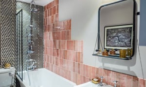 The bathroom with a shower over the bath, black and white tiles behind, and stepped pink tiles on the long wall