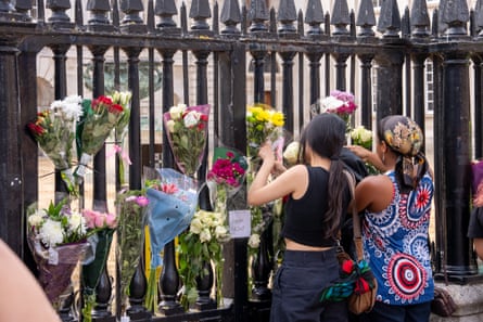 Two women attach bouquets of flowers to the iron gates of the Senate House