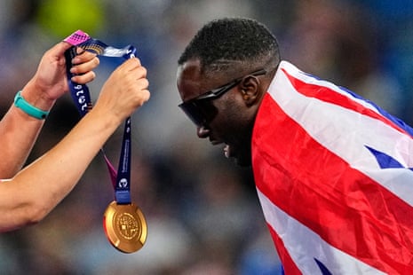 Britain's Romell Glave bends over to get his gold medal after winning the men's 100m final.