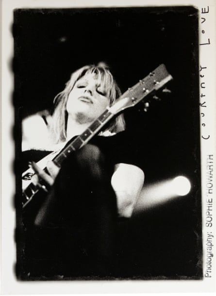 Black and white image of Courtney Love playing the guitar, shot from below