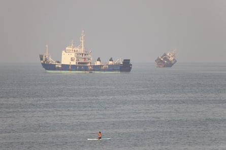 Two vessels in the sea, as a man in a canoe sails past in the foreground