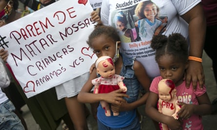 Children holding dolls covered with fake blood stand next to a sign that reads in Portuguese ‘Stop killing our children’.