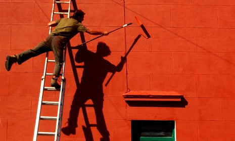 Man on ladder reaching across and balancing on one leg while painting wall