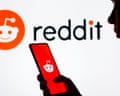 A person loading Reddit on their phone in front of a Reddit sign in the background