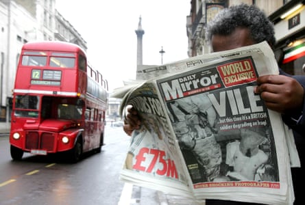 A man reading the Mirror newspaper, with a red London bus to the side of him