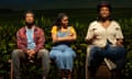 Three Black people sit in a row on a stage, one man and two women, wearing casual clothes.