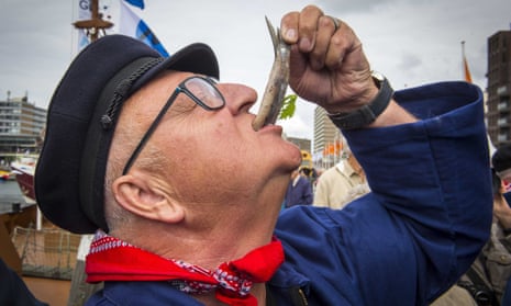 A visitor eats a fish during Vlaggetjesdag, the day on which traditionally the new herring is shipped into the harbour of Scheveningen, the Netherlands