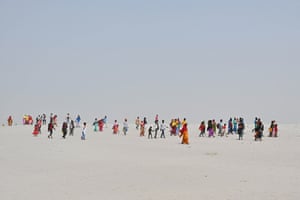 People in brightly coloured clothes walk across a barren landscape