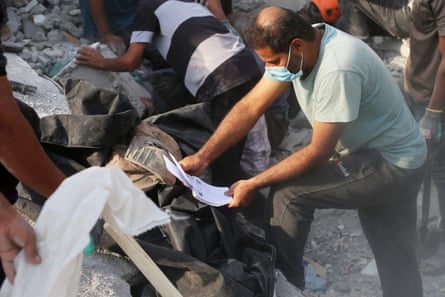 A man in a face mask holds a book while around him people dig through rubble