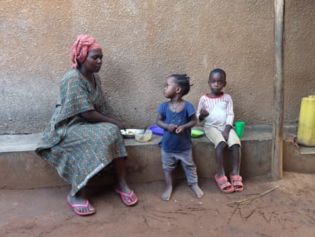 A woman sits on a bench sharing a plate of food with two children