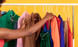 A person's arm is extended and touching a clothes hanger and a jacket. There are different coloured clothes, which are all on clothes hangers. The background is yellow