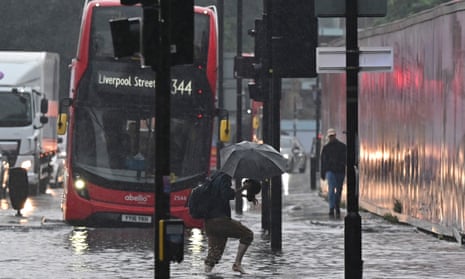 A pedestrian crosses through deep water on a flooded road in east London on 25 July