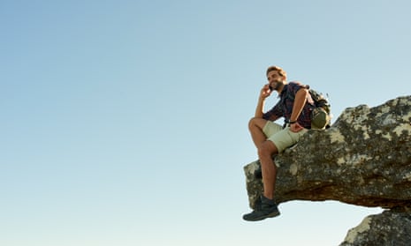 Shot of a hiker talking on his phone while sitting on the edge of a cliff
