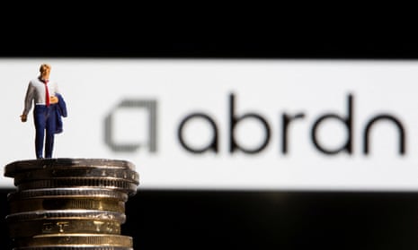 Businessman toy figure standing on UK pound coins in front of an abrdn logo.