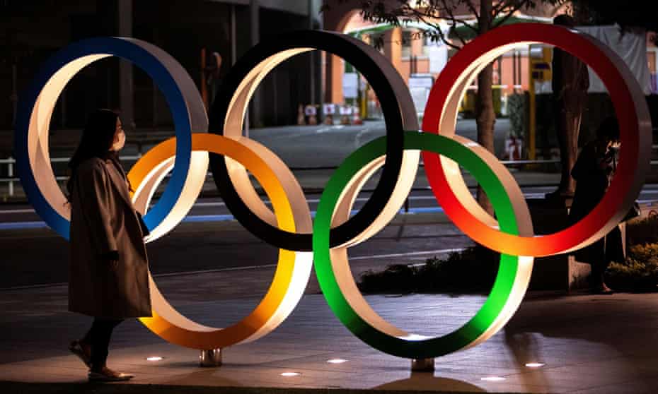 A woman wearing a protective face mask walks past the Olympic rings in front of the Japan Olympics Museum in Tokyo.
