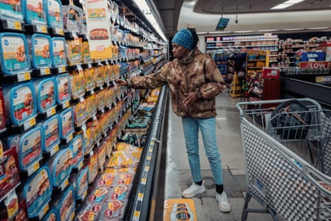 woman reaches for food in refrigerated section of grocery store