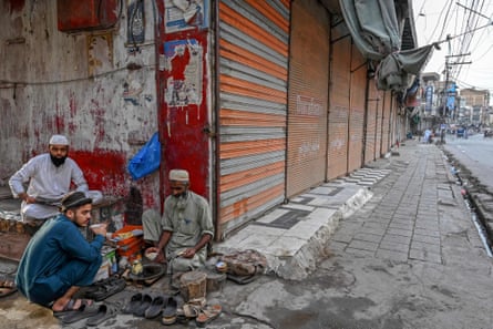 An old man drinks tea at his roadside stall with a younger man and a boy