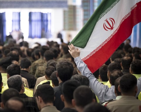 An Iranian man holds the country's flag while participating in a ceremony at the Imam Khomeini Grand Mosque in Tehran, Iran, on August 7, 2025, to commemorate the civilians and Islamic Revolutionary Guard Corps (IRGC) generals killed during the 12-day war between Iran and Israel