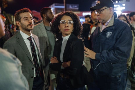 woman in blazer stands outside on city street at night with arms folded while looking ahead