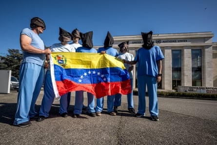 people stand in blue clothes with hoods over the heads while holding a Venezuelan flag