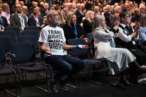 Andrew Boff, wearing a T-shirt reading “Trans rights are human rights”, holds out his hands and says something from a seat in the audience
