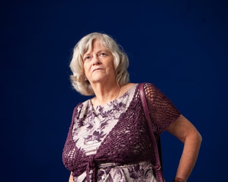 In a purple and white dress and standing before a blue background, Ann Widdecombe looks upwards