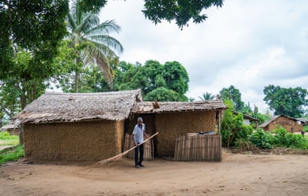 A man sweeping the ground outside his large mud hut with a long palm frond