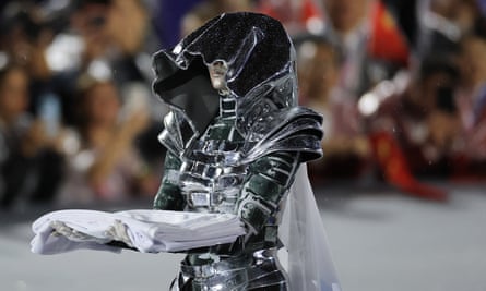 A woman in silver armour with a hood holding a folded flag in her arms