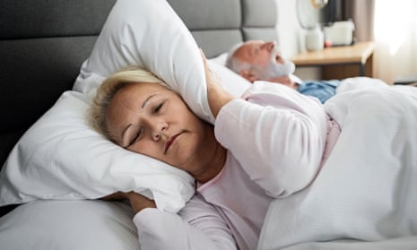 Wife blocks ears with pillow while husband snores