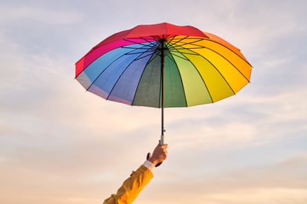 Arm holding colourful vivid rainbow umbrella at cloudy sky at sunset