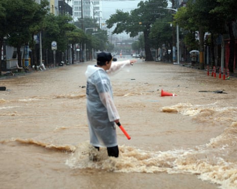 A police officer wades through deep floodwaters, directing traffic on a flooded street in Geoje