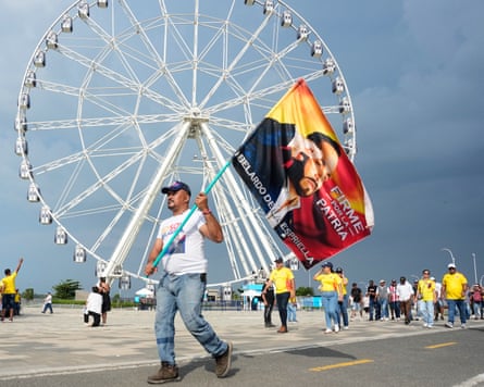 A man holding a flag on a pole depicting Espriella walks with others past a ferris wheel