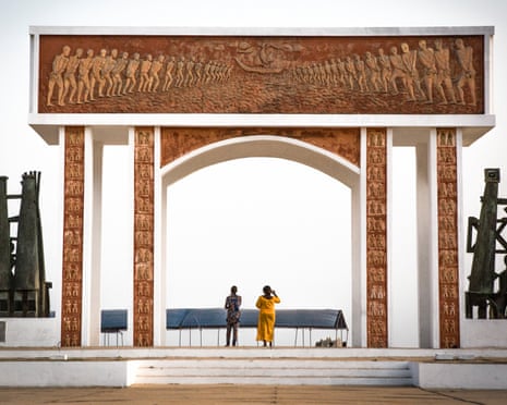 Two people stand under a large sculpted archway with abstract sculptures on either side