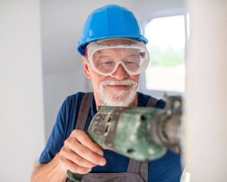 Man with a helmet, goggles and drill working indoors