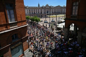 A large group of cyclists participating in the 11th stage of the Tour de France race through a narrow cobblestone street lined with spectators in Toulouse, France.