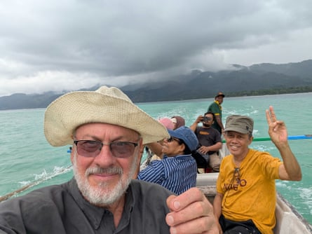 Tim Flannery takes a selfie with members of his team on a small boat on turquoise sea with mountains in the background