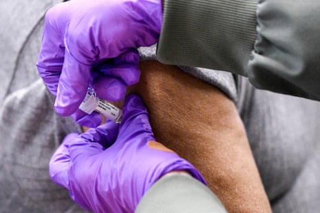 close up of a pair of gloved hands pressing a syringe into a person's arm