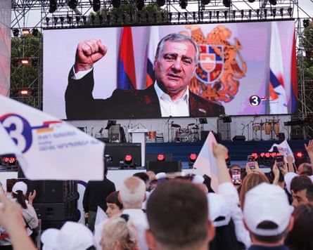 People with flags watch a large screen showing Samvel Karapetyan making a sign of strength with his fist