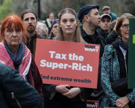 Uma mulher tem uma leitura de pôsteres: 'Tributação super rica. Termine a riqueza extrema" em uma manifestação