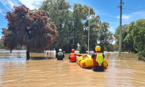 SES crews wade through hip-high brown flood waters while pulling along an inflatable rescue boat