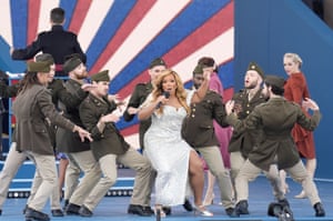The singer Marisha Wallace in a white dress surrounded by male dancers in uniform performs on stage